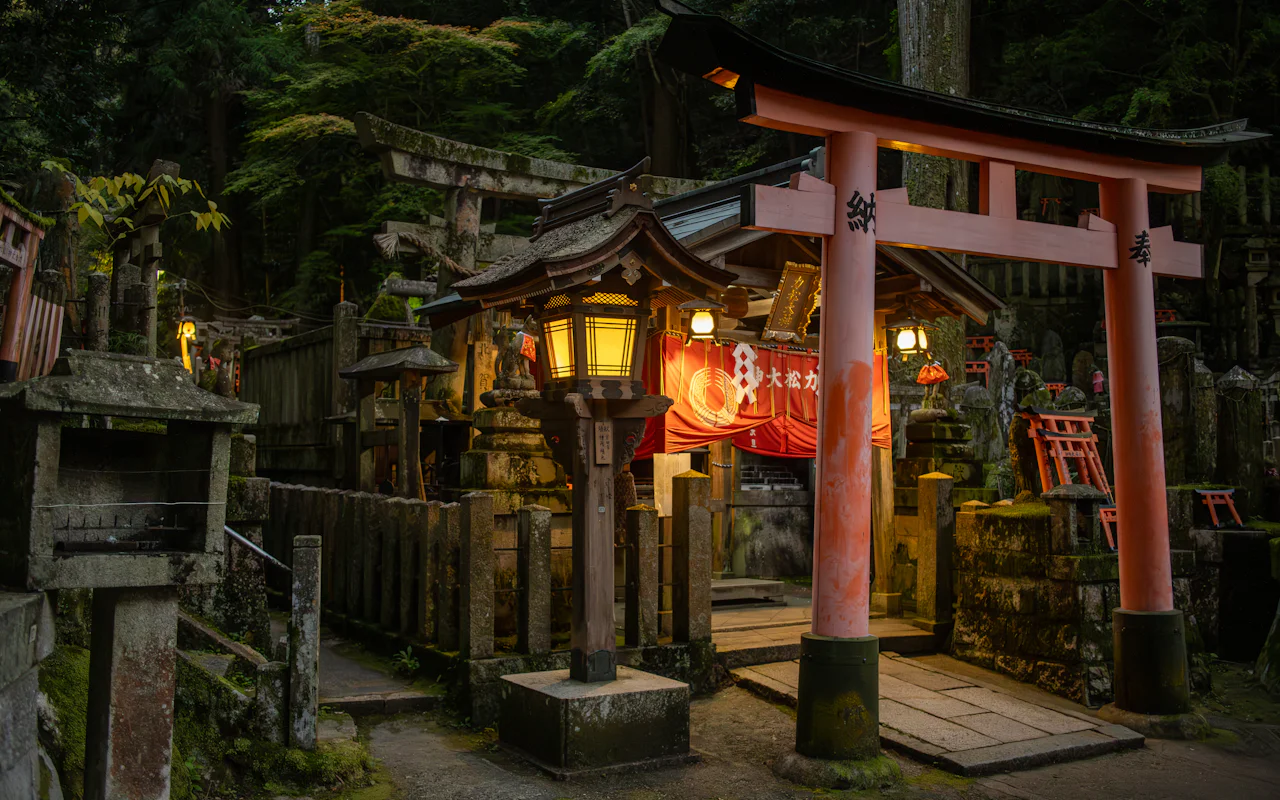 夕暮れに灯籠がともる神社の入口